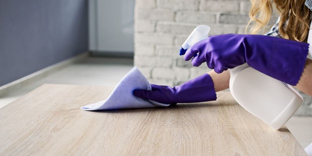 limpiar-y-desinfectar-mujer-con-guantes-desinfectando-superficie-de-la-casa-virus-insumosfirstpro.com